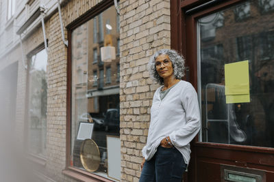 Portrait of senior female entrepreneur with hand in pocket standing outside store