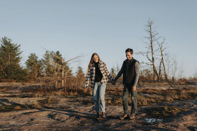 Young couple standing on field against sky