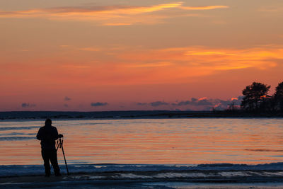 Rear view of silhouette man standing at beach during sunset