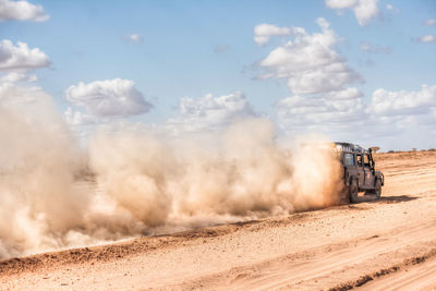 Scenic view of a 4wd car rushing through the desert  against a blue cloudy sky