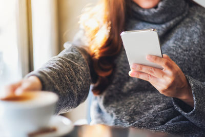 Midsection of woman using mobile phone while having coffee at shop