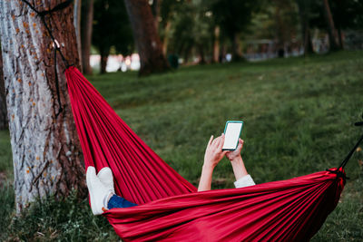 Woman using smart phone while lying in hammock at forest