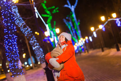 Portrait of woman standing against illuminated christmas tree at night