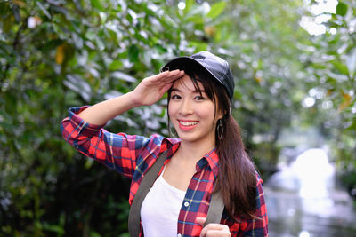 Portrait of smiling young woman standing against trees