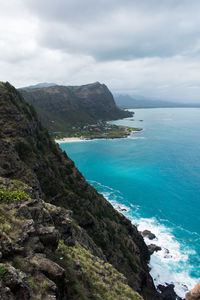 Scenic view of rocky mountains and blue sea against cloudy sky