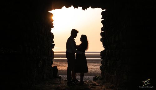 Silhouette couple with arms outstretched against sky during sunset