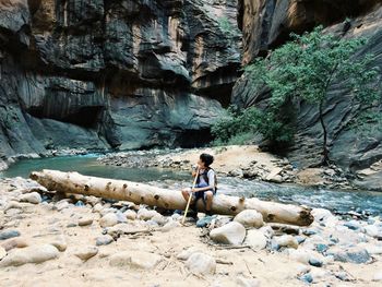 Boy sitting on log at lakeshore in forest