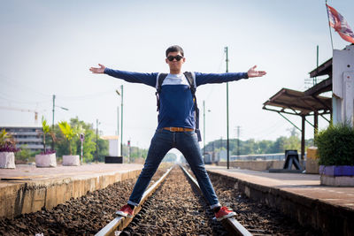Portrait of man with arms outstretched standing on railroad tracks