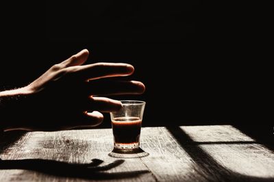 Cropped hand reaching towards coffee on table against black background