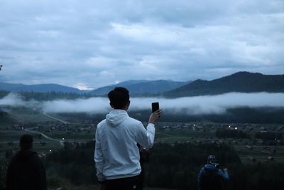 Rear view of man holding mobile phone while standing on mountain