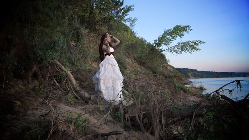 Woman standing by lake in forest against sky