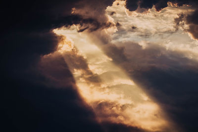 Low angle view of sunlight streaming through clouds