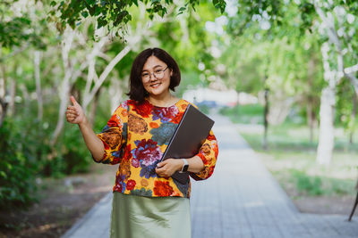 Portrait of smiling young woman standing against trees