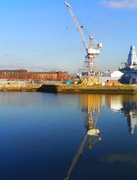 Reflection of cranes in water against sky