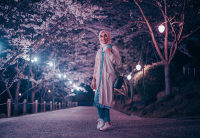 Portrait of woman standing against illuminated trees at night