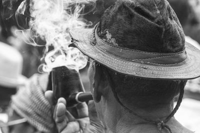 Close-up rear view of man wearing hat while smoking pipe outdoors