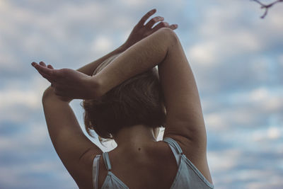 Rear view of woman with arms raised dancing against sky