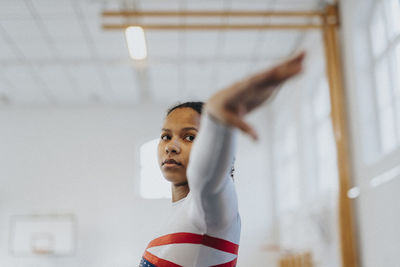 Dedicated teenage girl with arm outstretched practicing exercise in gym