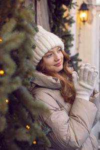 Portrait of young woman standing against illuminated christmas tree