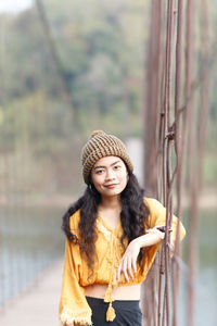 Portrait of young woman standing on footbridge over lake