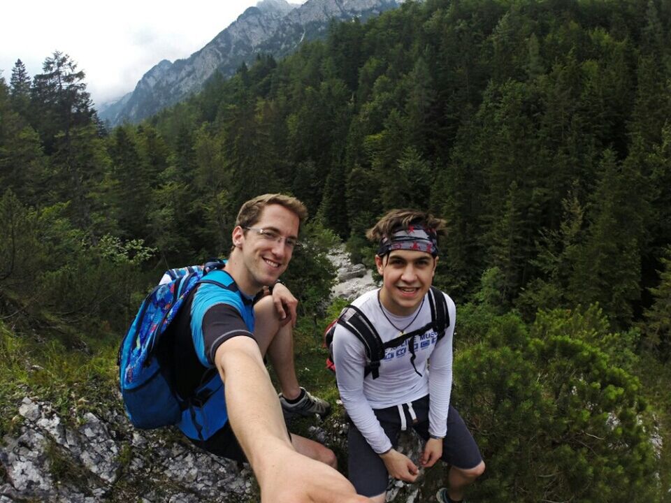 lifestyles, leisure activity, tree, mountain, casual clothing, person, young men, young adult, portrait, looking at camera, smiling, happiness, vacations, front view, standing, nature, forest, sitting