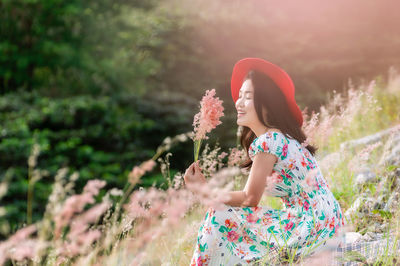 Side view of smiling woman sitting amidst flowering plants on field