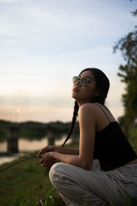 Side view of young woman looking away while sitting against sky