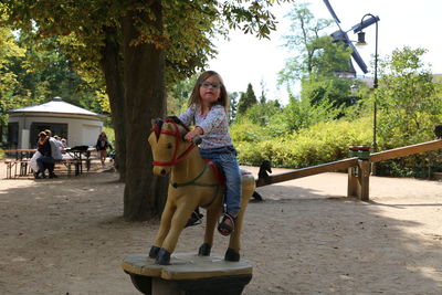 Full length portrait of girl sitting on rocking horse against trees