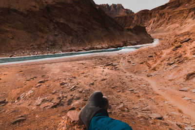 Low section of man resting on mountain against sky