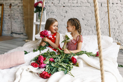 Smiling siblings sitting amidst flowers on bed at home