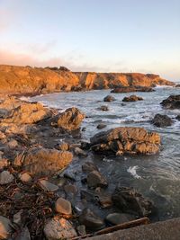 Rocks on beach against sky during sunset