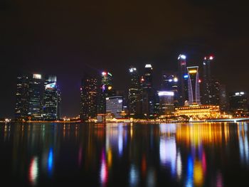 Illuminated buildings by river against sky at night