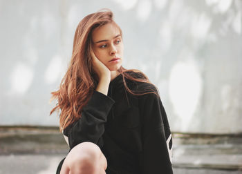 Sad beautiful woman sitting against wall