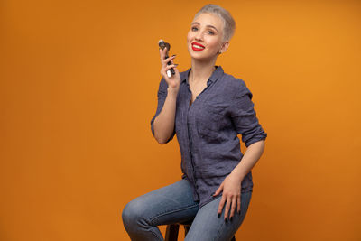 Smiling woman with make-up brushes sitting against orange background