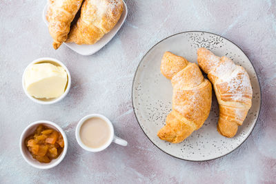 Fresh crispy croissants on plates, a cup of coffee and bowls with jam and butter 