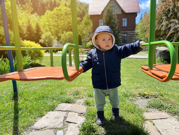 A cute boy of one and a half years standing near the swing. backyard of the house.