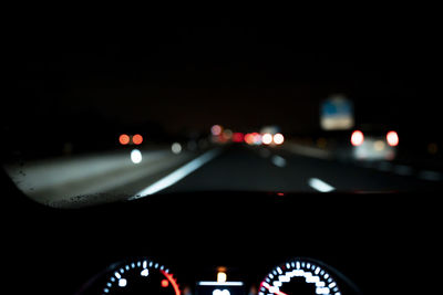 Blurred illuminated dashboard and view from windshield of car driving along asphalt highway at night
