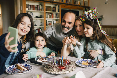 Boy taking selfie with family eating birthday cake while enjoying at home