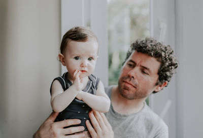 Portrait of a caucasian girl sitting in her father's arms with a pensive look to the side