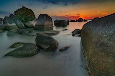 Rocks by sea against sky during sunset