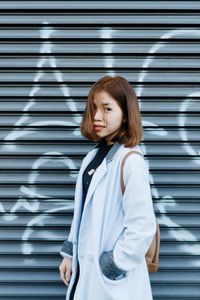 Portrait of young woman standing against shutter