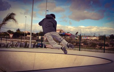 Rear view of man holding push scooter while jumping over sports ramp