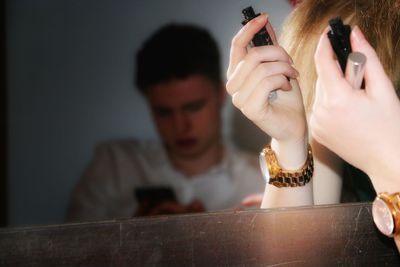 Cropped image of woman holding mascara with man reflecting on mirror