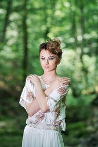 Portrait of young woman standing against trees