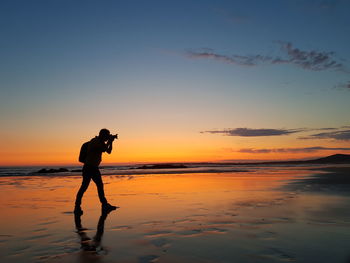 Silhouette man photographing at sunset