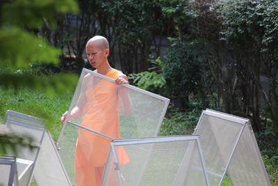 Monk holding netting equipment while standing against plants
