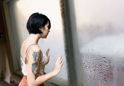 Side view of woman standing by wet window