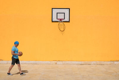 Side view of man playing basketball against yellow wall