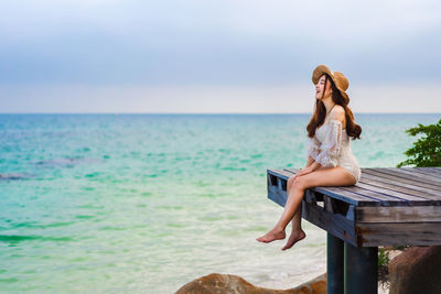 Woman sitting at beach against sky