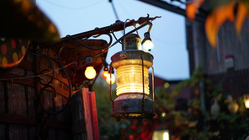 Low angle view of illuminated lamp hanging by building against sky